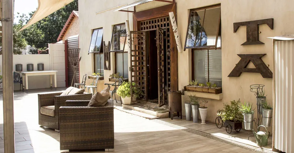 Sunlit courtyard entrance of Casa Lumini Guest House with wicker chairs and potted plants