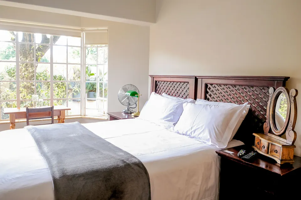 Double room with white bedding, carved headboard and bay window onto the garden