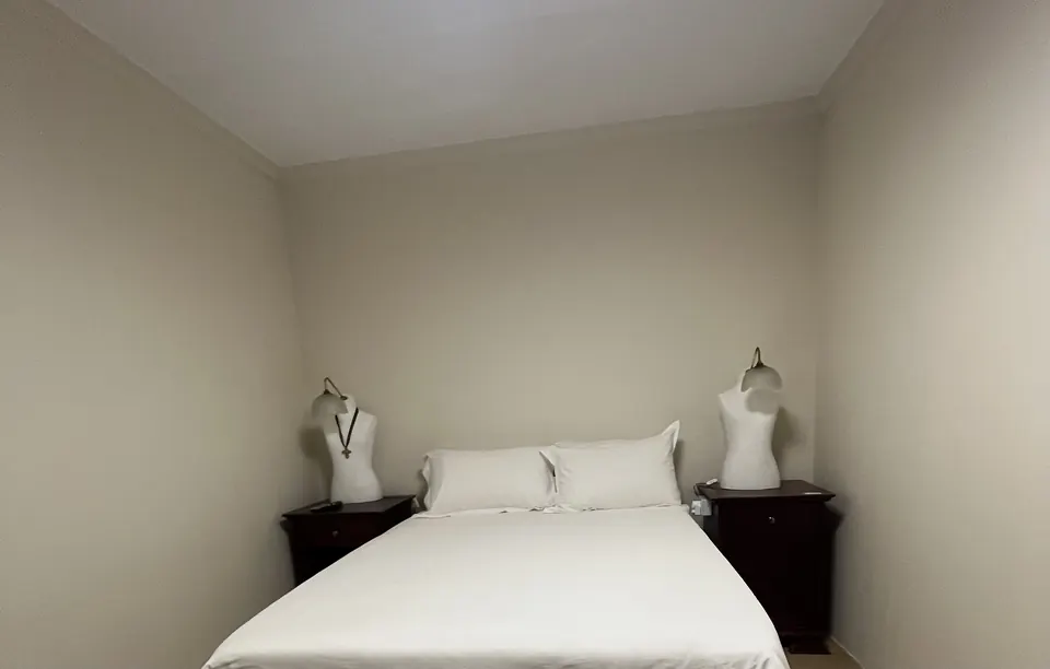 Double room with white bedding flanked by sculptural bust lamps on dark bedside tables
