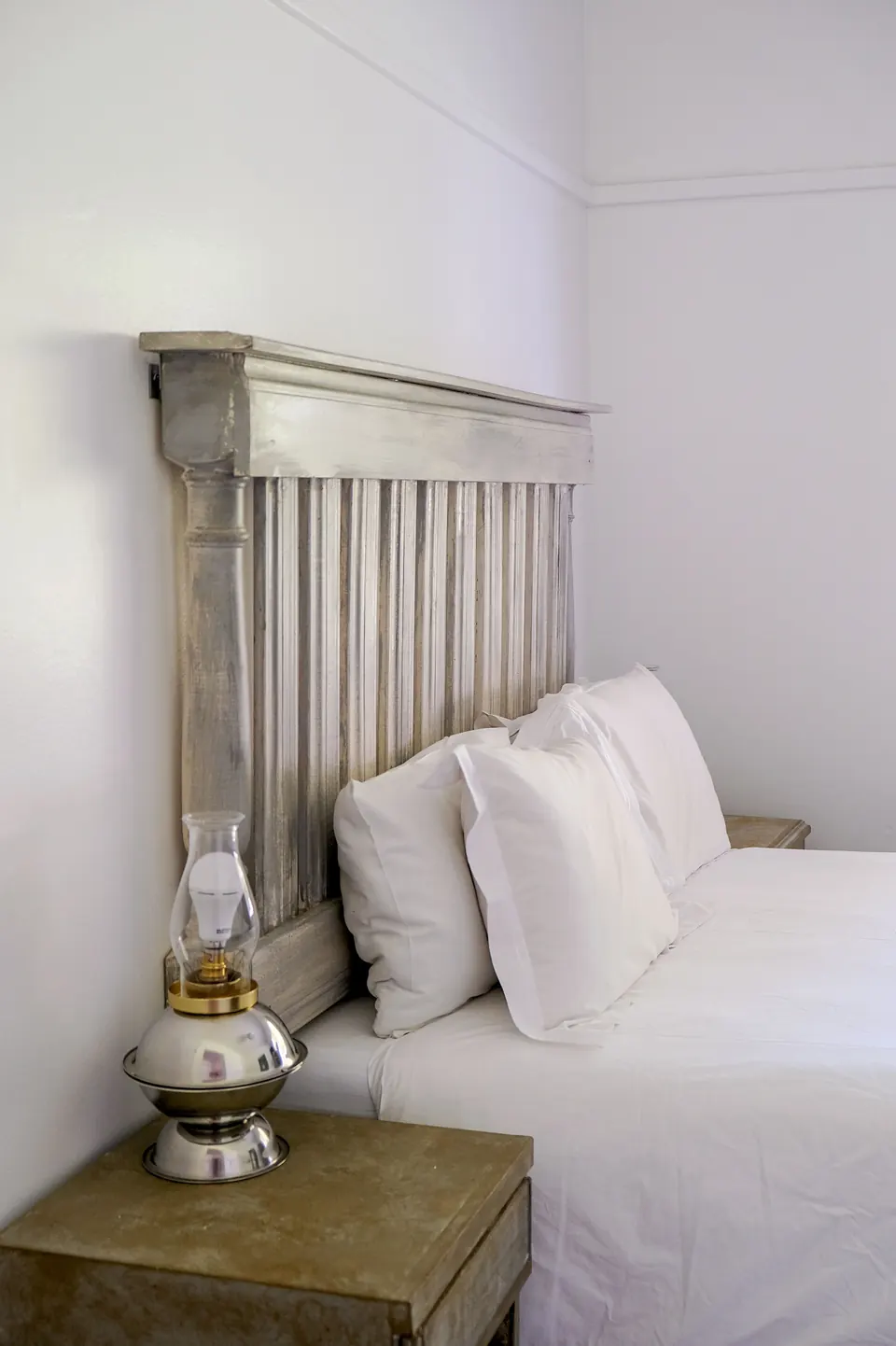 Grey timber headboard and brass oil lamp beside a crisp white bed