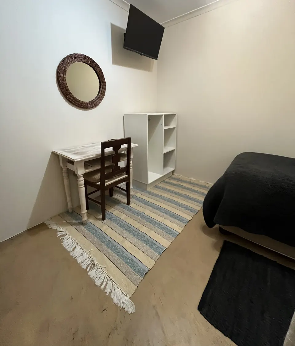 Single room with whitewashed desk, round mirror and wall-mounted TV