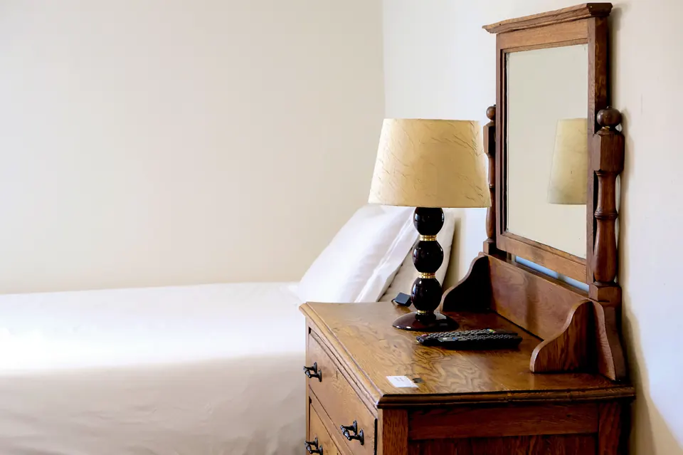 Bed beside an antique dresser with mirror and lamp