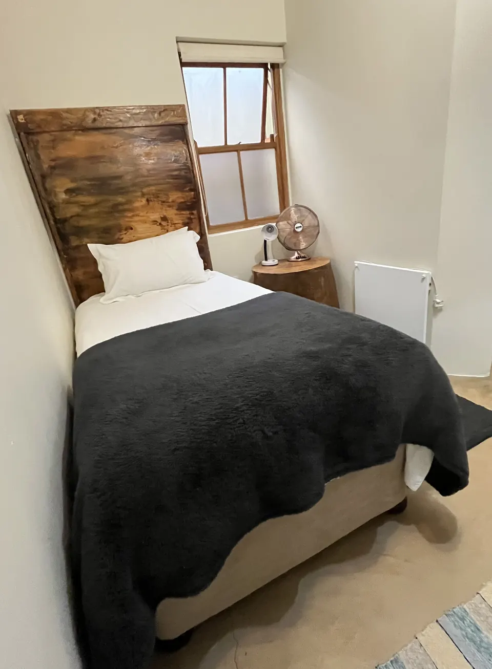 Single room with rustic timber headboard, dark throw and wooden side table